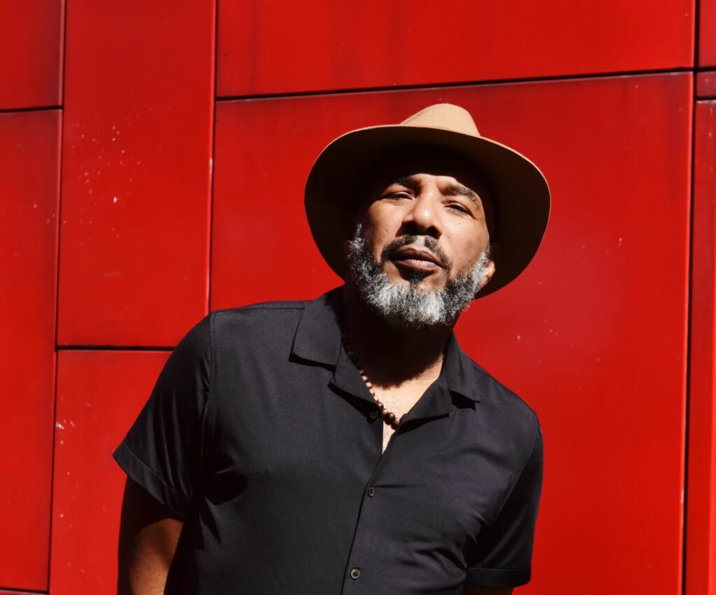 Portrait d'Anthony Joseph avec un chapeau et sur fond rouge