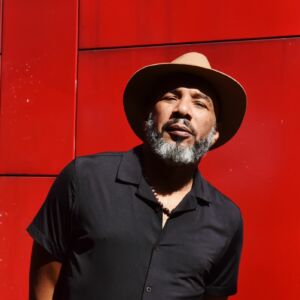 Portrait d'Anthony Joseph avec un chapeau et sur fond rouge